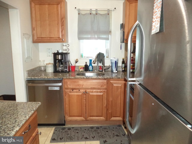 kitchen featuring a sink, dark stone countertops, light tile patterned flooring, and stainless steel appliances