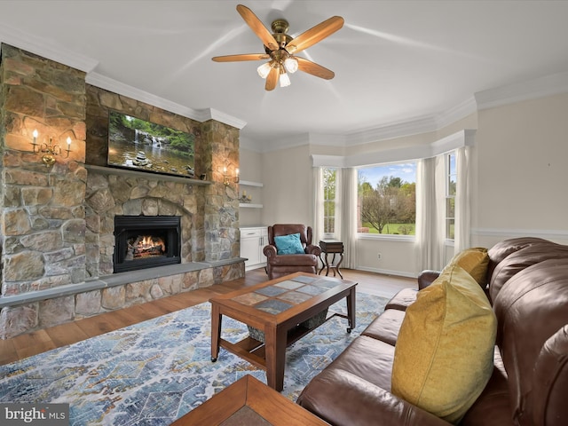 living room featuring crown molding, a stone fireplace, a ceiling fan, and wood finished floors