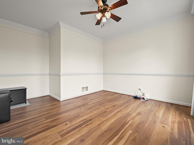 empty room with wood finished floors, visible vents, a ceiling fan, ornamental molding, and baseboards