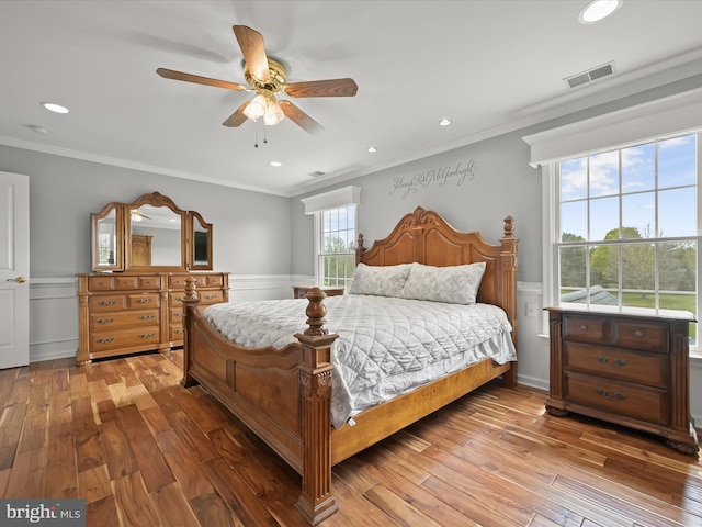 bedroom with wainscoting, visible vents, light wood finished floors, and crown molding