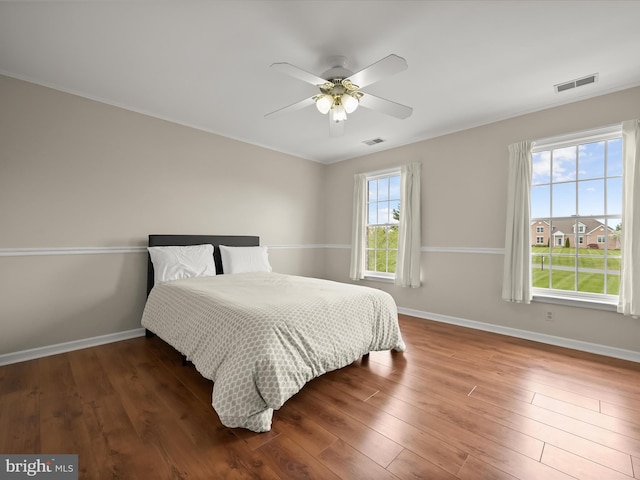 bedroom featuring wood finished floors, visible vents, a ceiling fan, and baseboards