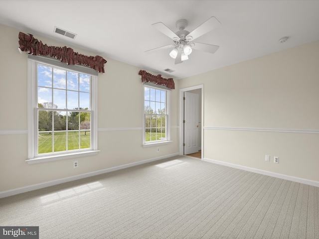 carpeted empty room with baseboards, a ceiling fan, and visible vents