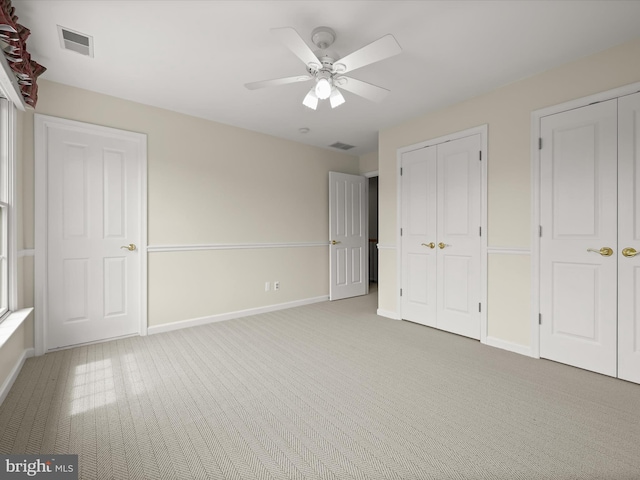 unfurnished bedroom with two closets, baseboards, visible vents, and carpet
