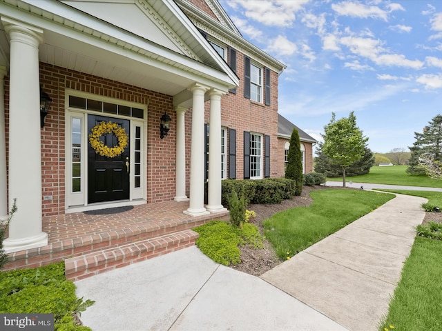 property entrance with brick siding, a yard, and covered porch