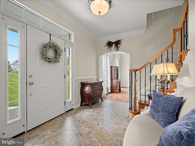 foyer entrance featuring wainscoting, arched walkways, ornamental molding, and stairs