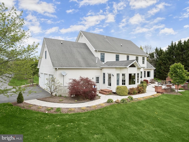 rear view of property featuring roof with shingles, a garage, a yard, a patio, and aphalt driveway