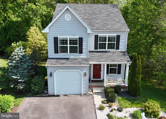view of front of home with roof with shingles, covered porch, a garage, and driveway