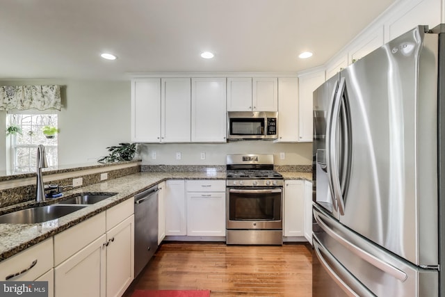kitchen featuring appliances with stainless steel finishes, a sink, white cabinets, recessed lighting, and light stone countertops