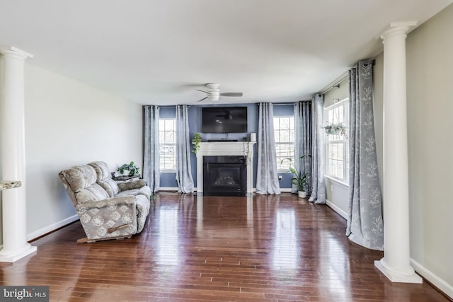 sitting room featuring a glass covered fireplace, healthy amount of natural light, wood finished floors, and decorative columns