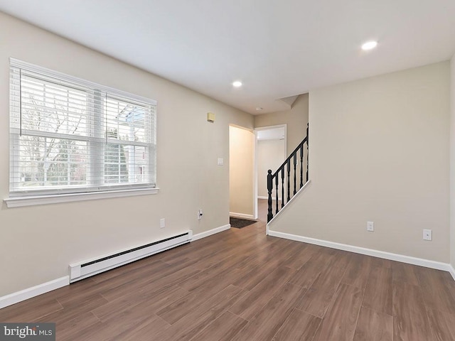 spare room featuring baseboard heating, wood finished floors, baseboards, and stairway