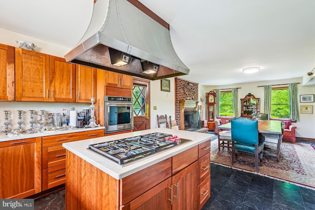 kitchen featuring stainless steel appliances, island exhaust hood, a brick fireplace, open floor plan, and light countertops