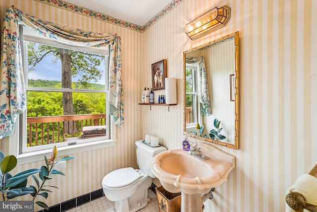 bathroom with toilet, tile patterned floors, wallpapered walls, and a sink