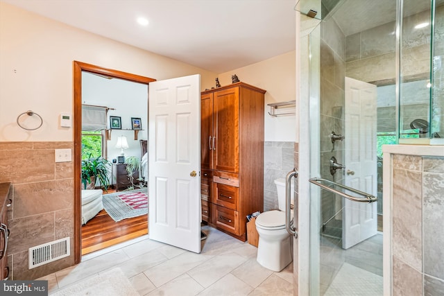ensuite bathroom with a shower stall, tile walls, tile patterned flooring, and visible vents