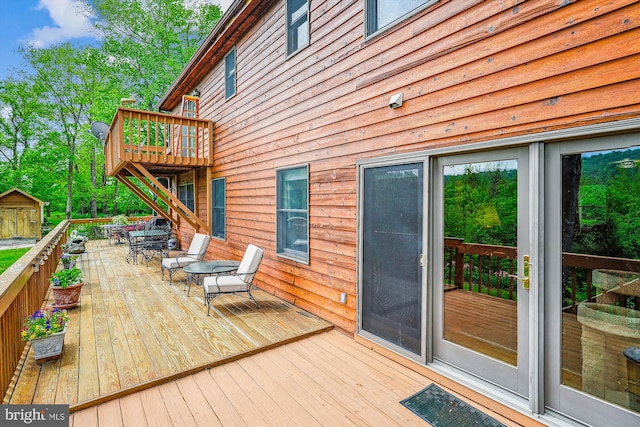 wooden terrace with an outdoor structure, outdoor dining area, and a storage shed