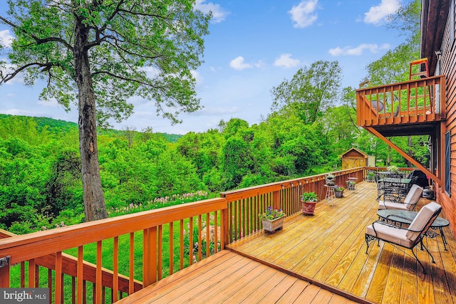 wooden terrace with an outbuilding, a forest view, and a storage unit