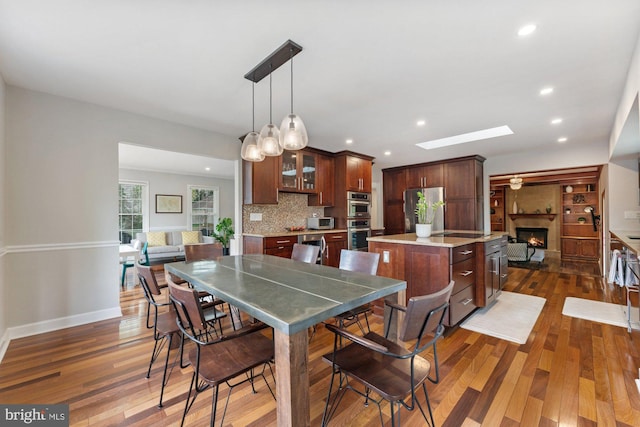 dining room with a lit fireplace, dark wood-type flooring, recessed lighting, and baseboards