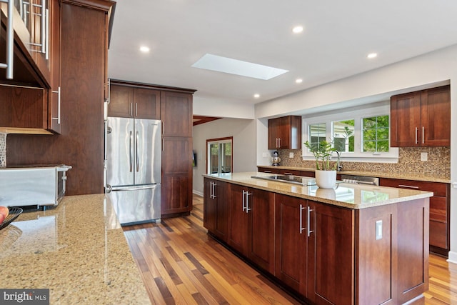 kitchen with stainless steel appliances, a skylight, backsplash, light wood-style floors, and a kitchen island