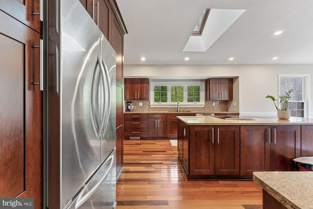 kitchen with stainless steel refrigerator, a sink, light wood-style flooring, a skylight, and decorative backsplash