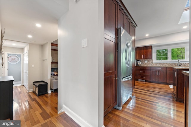kitchen featuring stainless steel fridge, light wood finished floors, a sink, decorative backsplash, and baseboards