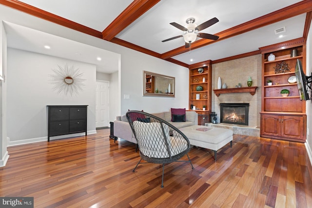 living room with beam ceiling, wood finished floors, a ceiling fan, a fireplace, and baseboards