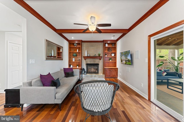 living area with wood finished floors, ceiling fan, a fireplace, baseboards, and crown molding