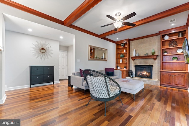 living room with beamed ceiling, baseboards, wood finished floors, a ceiling fan, and a fireplace
