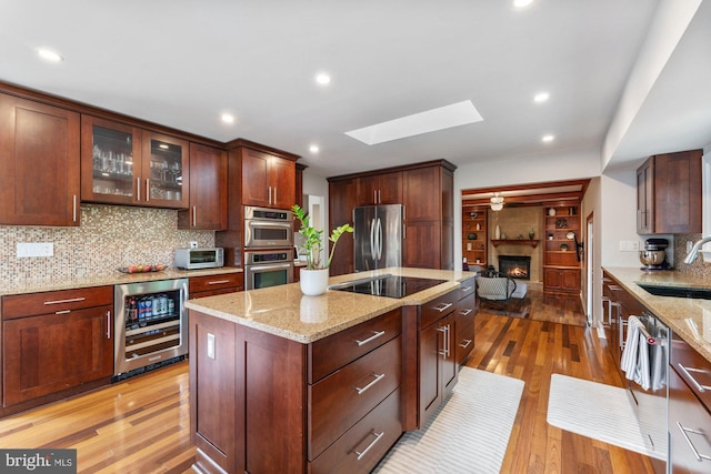 kitchen featuring beverage cooler, appliances with stainless steel finishes, a sink, a skylight, and a lit fireplace
