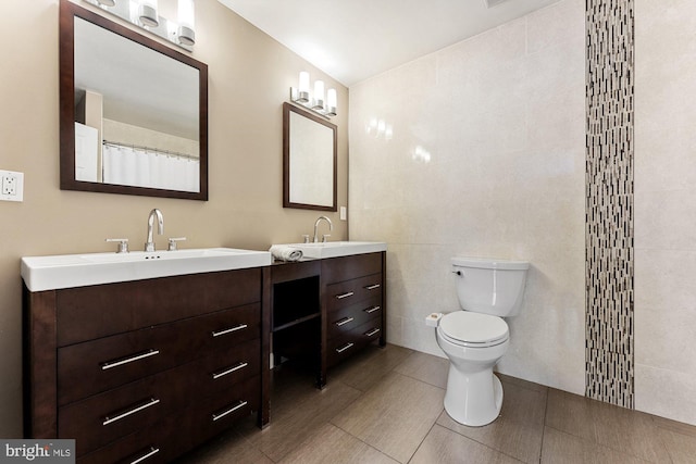 full bath with tile walls, two vanities, tile patterned floors, toilet, and a shower with curtain