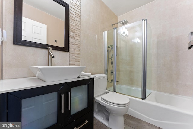 bathroom with toilet, combined bath / shower with glass door, vanity, tile patterned floors, and tile walls