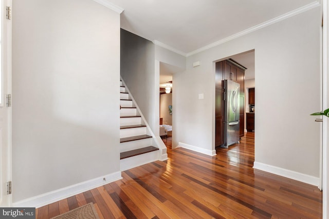 stairs with wood finished floors, crown molding, and baseboards
