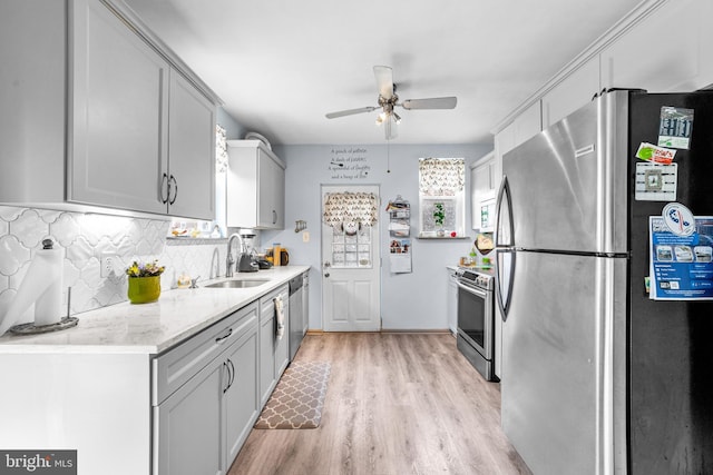 kitchen featuring light wood-style flooring, decorative backsplash, stainless steel appliances, a sink, and ceiling fan