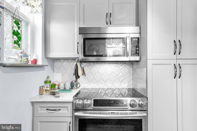 kitchen featuring stainless steel appliances, light stone countertops, white cabinets, and backsplash