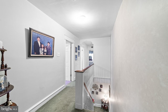hall featuring arched walkways, an upstairs landing, baseboards, and carpet floors