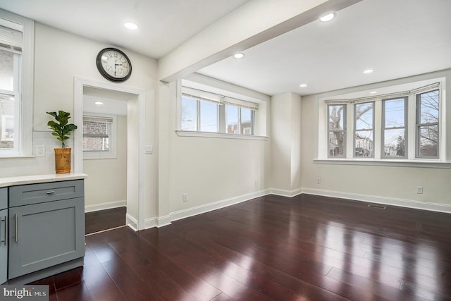 unfurnished living room with a wealth of natural light, recessed lighting, baseboards, and dark wood-type flooring