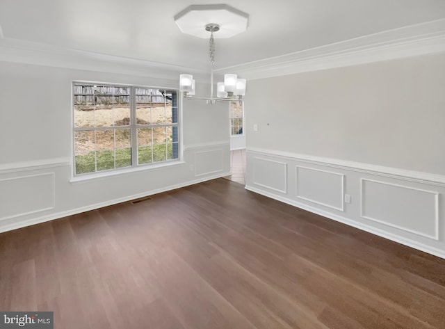 unfurnished dining area with dark wood-style flooring, ornamental molding, a chandelier, visible vents, and wainscoting