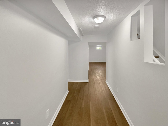 corridor featuring baseboards, a textured ceiling, and wood finished floors
