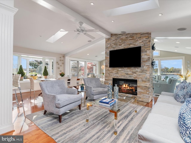 living area with plenty of natural light, vaulted ceiling with skylight, and a stone fireplace