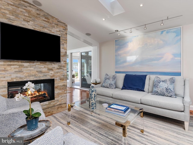 living room with track lighting, a skylight, wood finished floors, and a fireplace