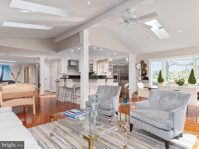 living room with wood finished floors, decorative columns, a ceiling fan, and lofted ceiling with skylight