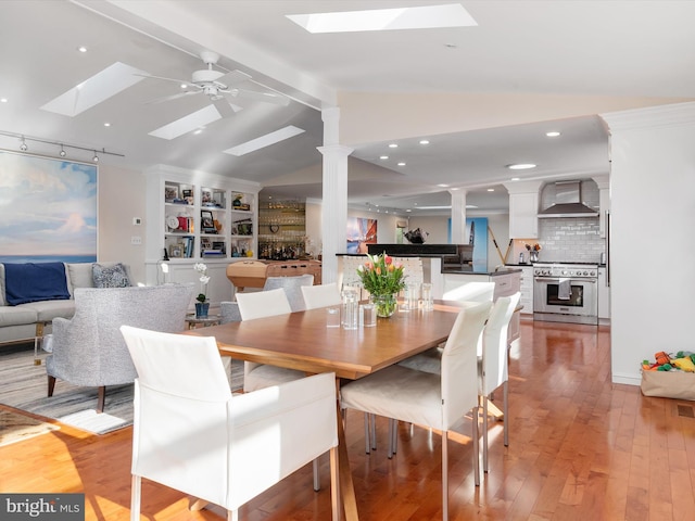 dining area featuring vaulted ceiling with skylight, light wood-style floors, ornate columns, and ceiling fan