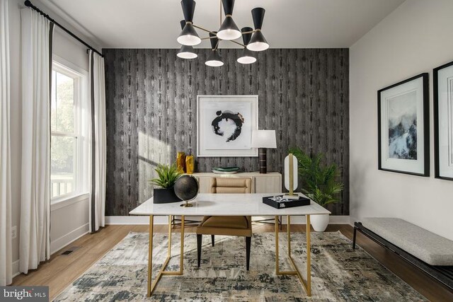 office area featuring light wood finished floors, a wealth of natural light, a notable chandelier, and an accent wall