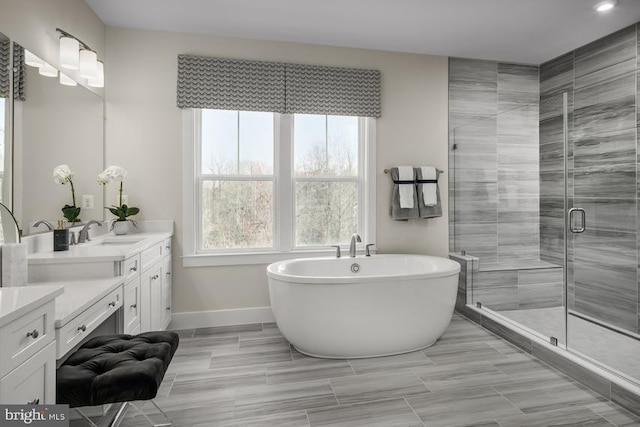 full bathroom featuring a stall shower, a sink, a soaking tub, baseboards, and double vanity