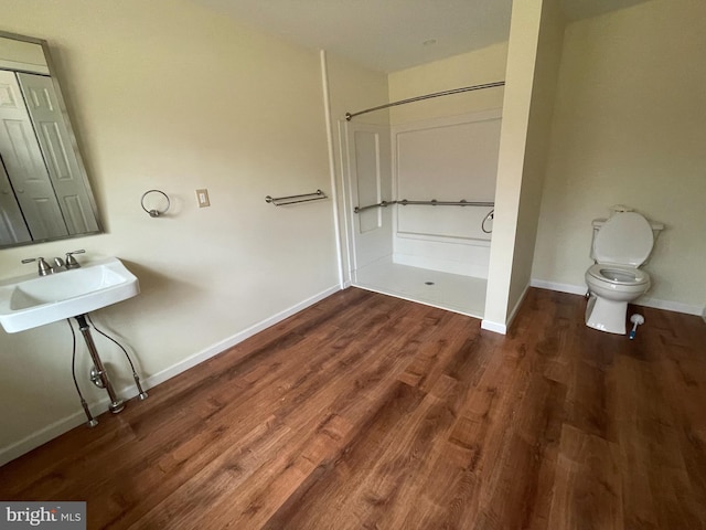 bathroom featuring baseboards, wood finished floors, toilet, and walk in shower
