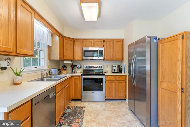 kitchen featuring stainless steel appliances, a sink, light countertops, and brown cabinets