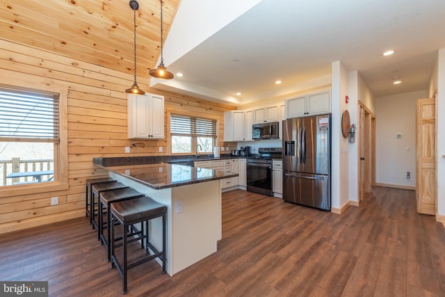 kitchen featuring stainless steel appliances, a sink, dark wood-style floors, wooden walls, and a peninsula
