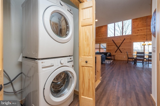 laundry room with stacked washing maching and dryer, wood walls, laundry area, and dark wood-style floors