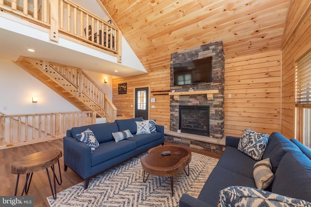 living room with wood walls, stairs, a towering ceiling, wood finished floors, and a stone fireplace