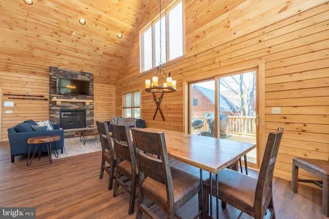 dining area featuring high vaulted ceiling, a chandelier, wooden walls, wood finished floors, and a stone fireplace