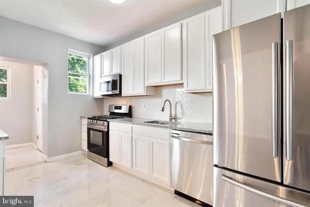 kitchen with appliances with stainless steel finishes, a sink, light stone countertops, light marble finish floors, and white cabinetry