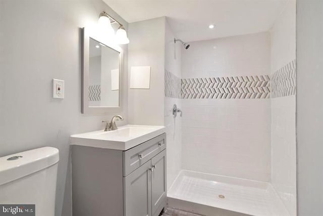 full bath with a tile shower, toilet, and vanity